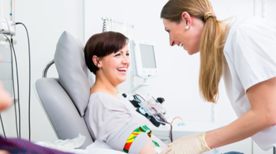 A smiling woman in a donation chair being prepared for a blood donation by a MBC phlebotomist.
